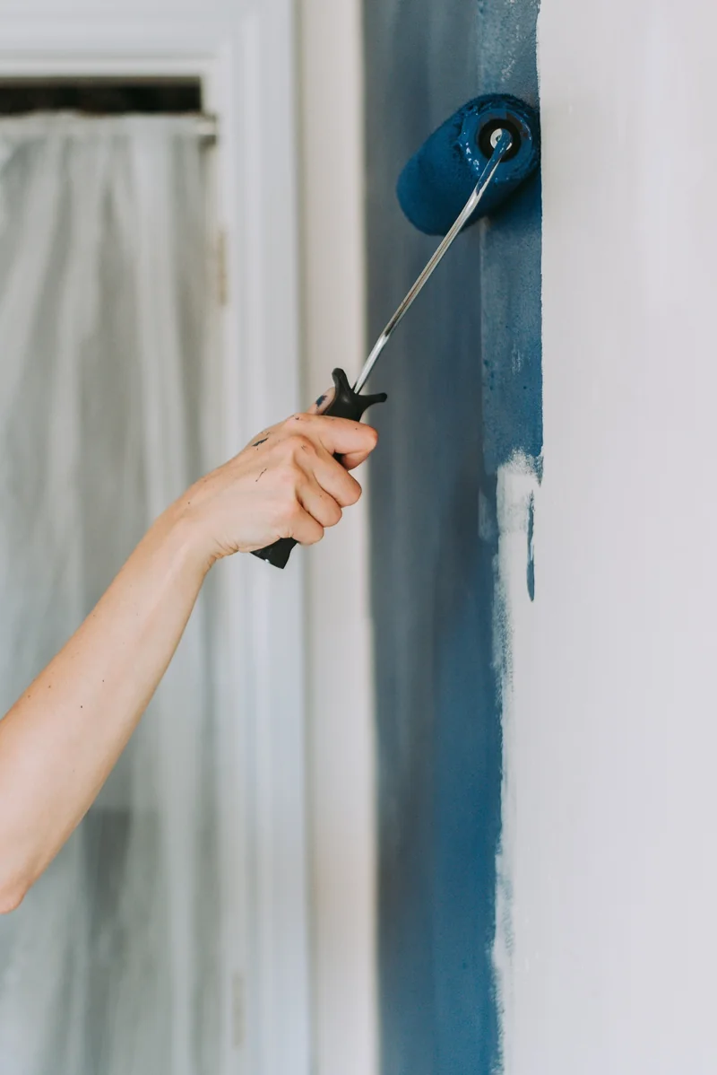 A painter applying a deep blue coat to a white interior wall.
