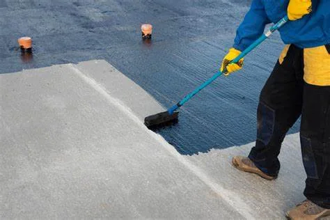 A worker applying waterproofing with a long-handled roller.